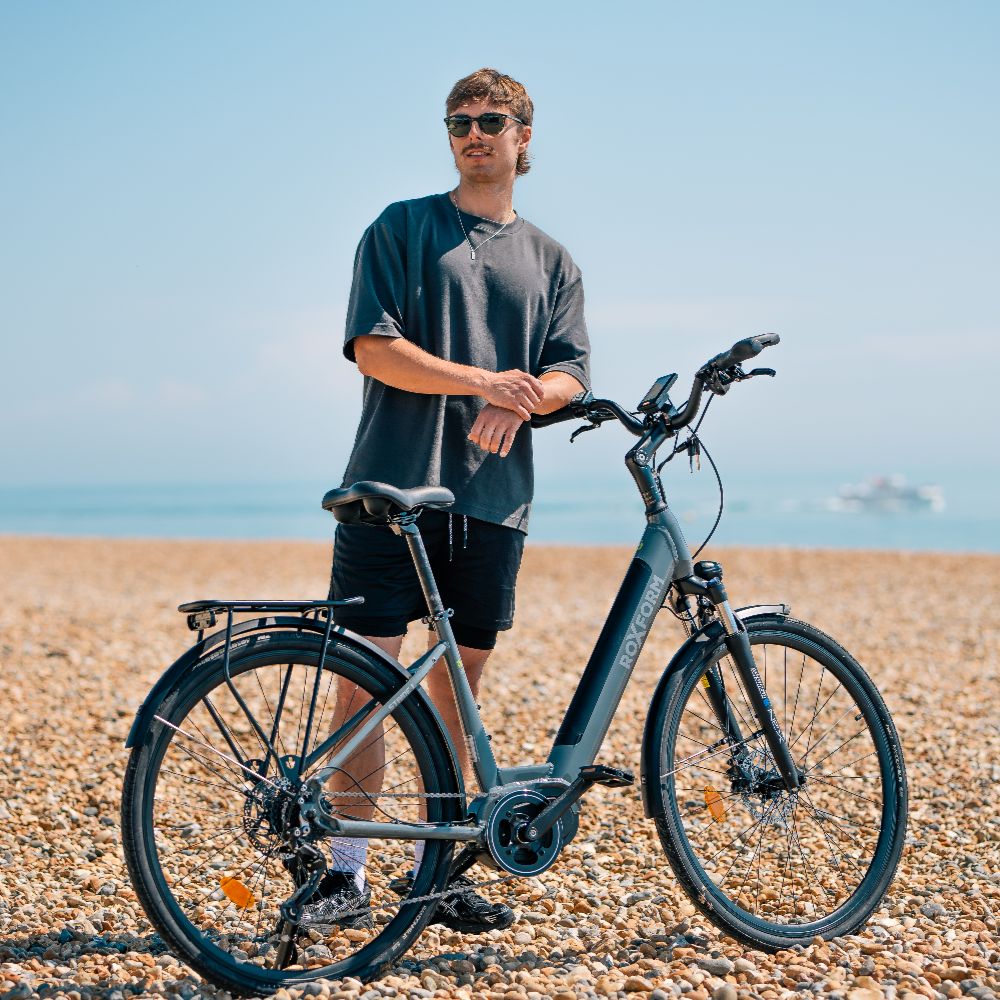 Roxform_Stride_L_e-bike lifestyle Man standing on a pebbly beach, wearing sunglasses and casual clothing.