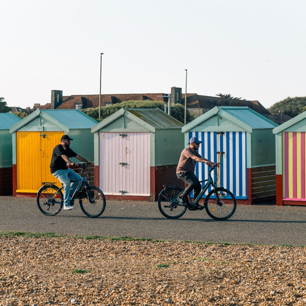 Roxform Valor S e-bike lifestyle image Two people riding on a path with colorful beach huts in the background.