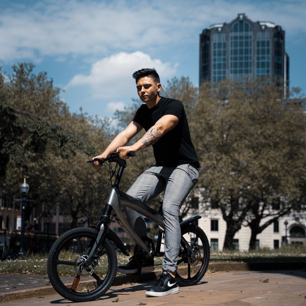 Cruzaa City e-bike lifestyle image of a Man riding in an urban park with buildings in the background
