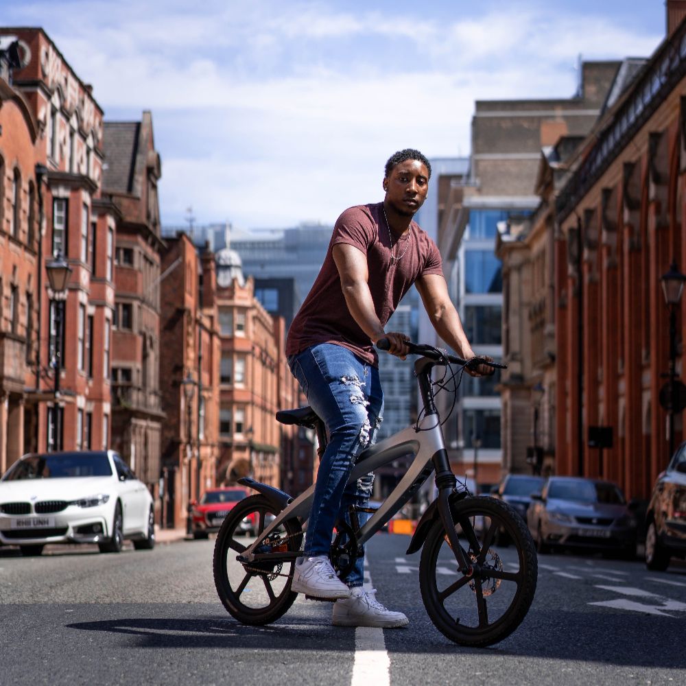 Cruzaa City e-bike lifestyle image of a Man riding on a city street with buildings and cars in the background