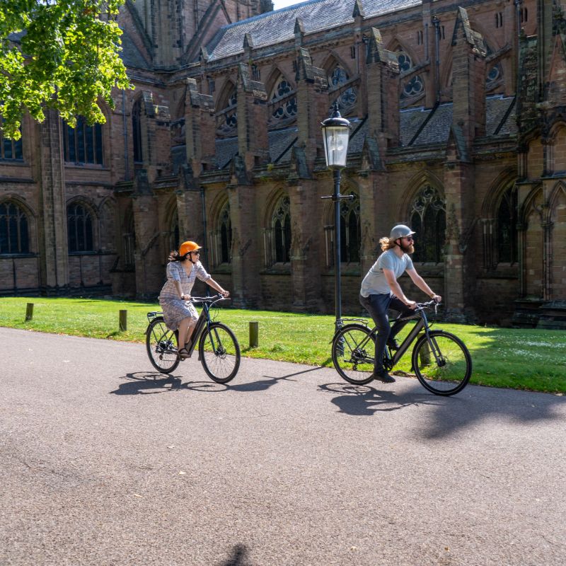 Dawes Scenic Crossbar ebike lifestyle Two people riding electric bikes in front of a large cathedral.