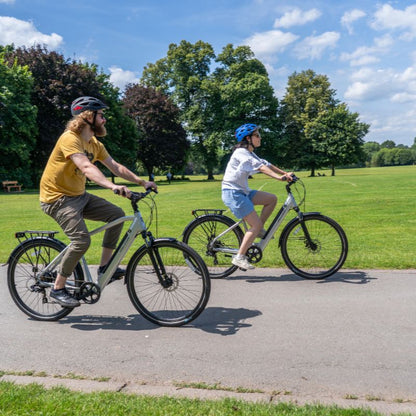 Falcon Horizon Low Step e-bike lifestyle Two people riding on a path in a park with trees and grass in the background.