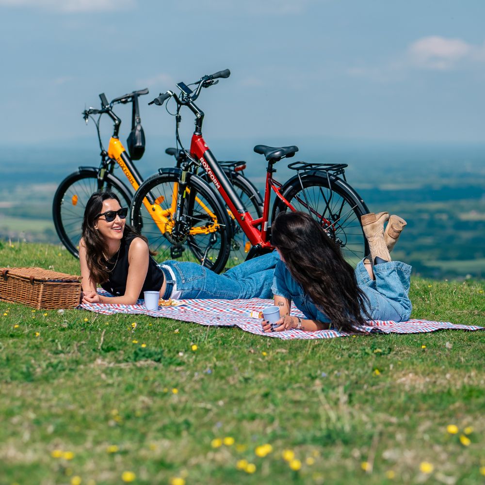 Roxform Stride S e-bike red and orange lifestyle image Two people relaxing on a blanket in a scenic outdoor setting.