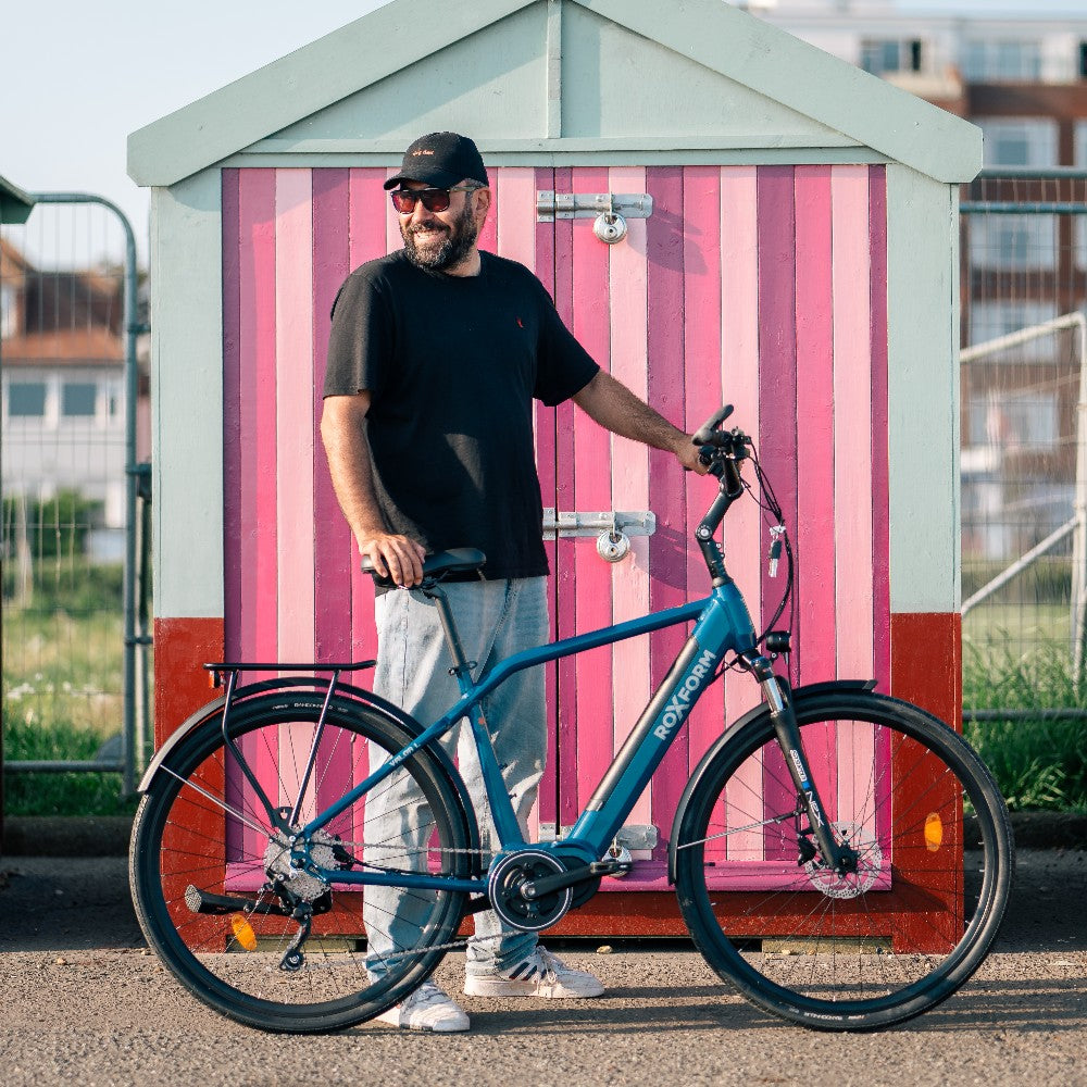 Roxform Valor L e-bike lifestyle image Man standing in front of a pink and white striped beach hut