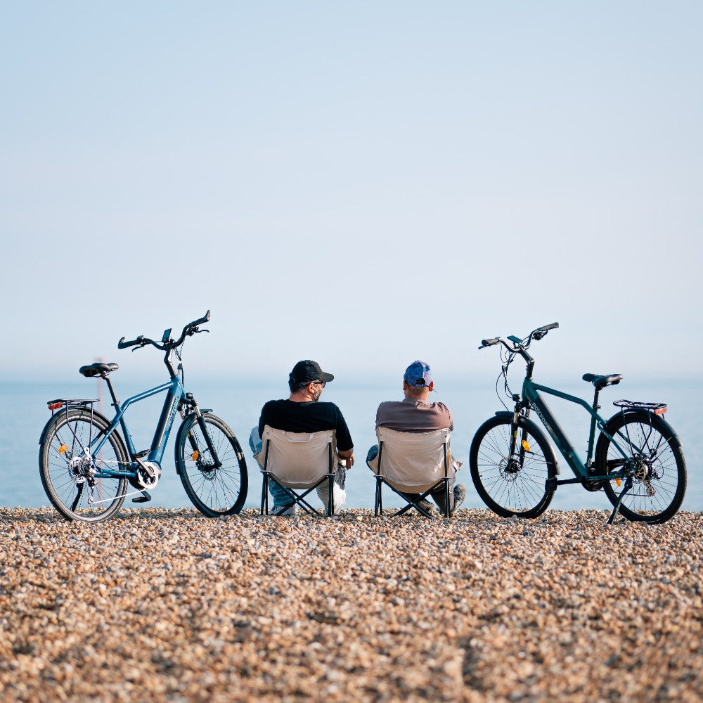Roxform Valor L e-bike lifestyle image beach Two people sitting on chairs with electric bicycles on a pebble beach.
