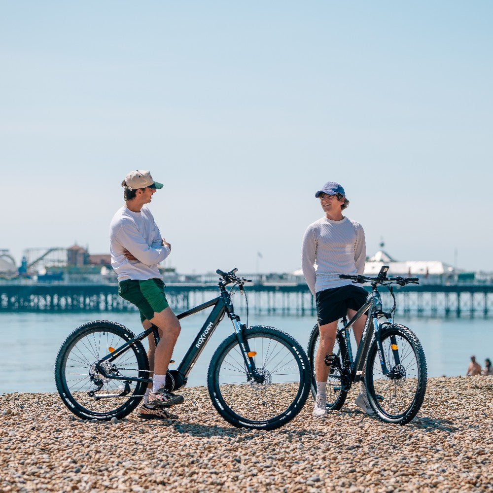 Roxform Venturis eMTB blue lifestyle on a pebbly beach with a clear sky.