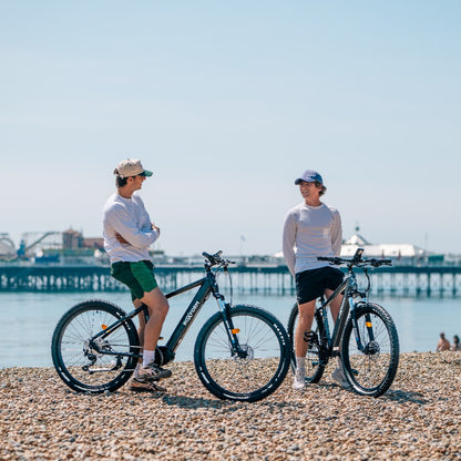 Roxform Venturis eMTB blue lifestyle on a pebbly beach with a clear sky.
