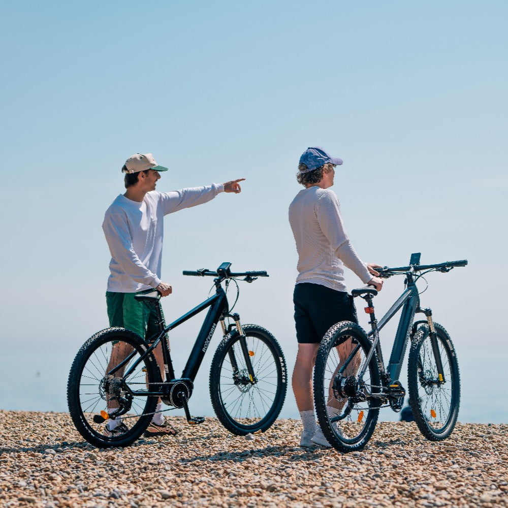 Roxform Venturis eMTB blue lifestyle Two people on a pebbly beach under a clear blue sky.