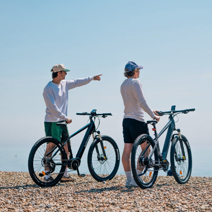 Roxform Venturis eMTB blue lifestyle Two people on a pebbly beach under a clear blue sky.