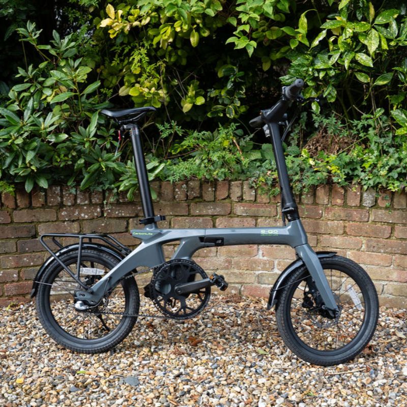 e-go CarbonLite3S lifestyle side view on a gravel path with greenery and a brick wall in the background
